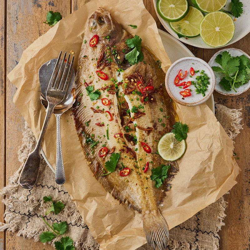 A whole, cooked witch sole on baking paper garnished with lime, chilli and coriander