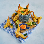 Tempura style prawns filling a bowl with some arranged across a wooden chopping board too