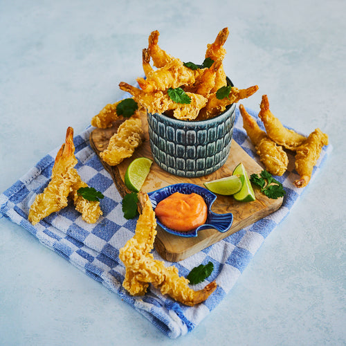 Tempura style prawns filling a bowl with some arranged across a wooden chopping board too