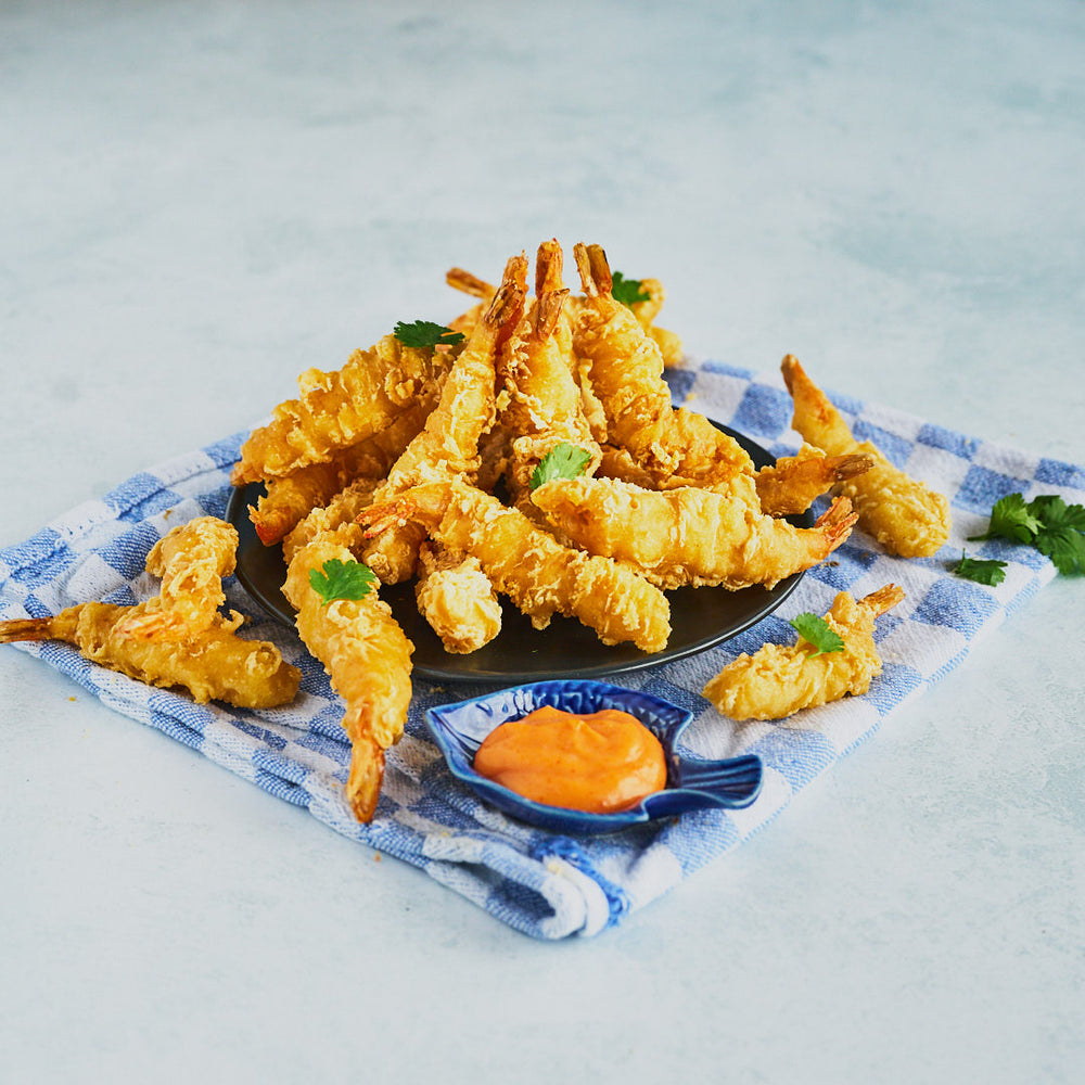 Tempura Prawns arranged in a tower on a black plate with a dipping sauce